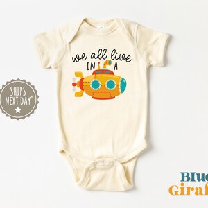 May include: A white baby onesie with a yellow submarine illustration and the text "we all live in a".