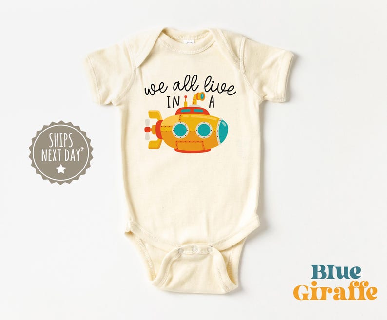 May include: A white baby onesie with a yellow submarine illustration and the text "we all live in a".