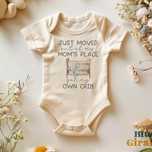 May include: A cream-colored baby onesie with the text "JUST MOVED out of my MOM'S PLACE got my OWN CRIB". A watercolor illustration of a crib with a blanket is above the text.