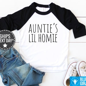 Peut inclure: T-shirt de baseball blanc et noir avec le texte "Auntie's Lil Homie" imprimé en noir sur le devant.