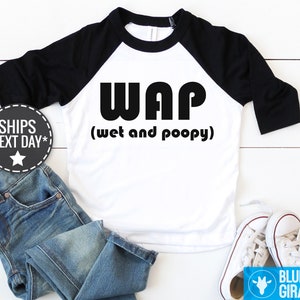 以下が含まれることがあります： 白と黒のベースボールTシャツに、黒で「WAP（ウェットアンドプーピー）」の文字が書かれています。シャツは黒のラグランスリーブです。