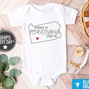 May include: White baby onesie with a black outline of the state of Pennsylvania and the text "Someone in Pennsylvania Loves Me" with a red heart.