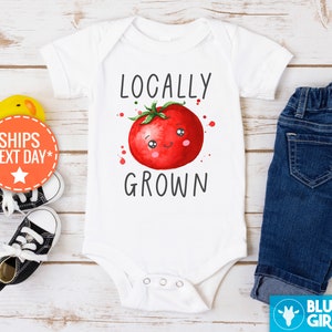 May include: White baby onesie with a red tomato illustration and the text "Locally Grown".