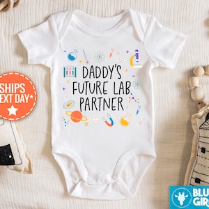 May include: White baby onesie with a colorful science theme. The onesie says "Daddy's Future Lab Partner" with various science icons surrounding the text.