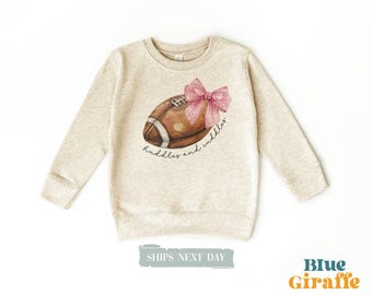 May include: A beige sweatshirt with a brown and white football with a pink bow on top. The text "huddles and cuddles" is printed on the sweatshirt.