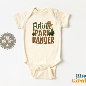 May include: A cream-colored baby onesie with the text "Future Park Ranger" in brown lettering. A green pine tree and a brown ranger hat are on either side of the text.
