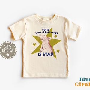 May include: Cream-colored t-shirt featuring a rat illustration inside a green star with the text "RATS SPELLED BACKWARDS IS STAR" in blue and green. The shirt has short sleeves and a crew neck.