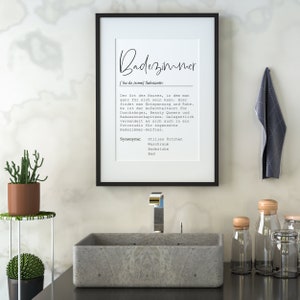 May include: A black framed print with the word "Badezimmer" in white text. The print is hanging on a white wall above a gray rectangular sink with a chrome faucet. There are two small glass jars with wooden lids on the counter to the right of the sink.