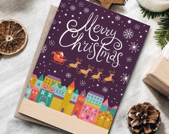 Puede incluir: Una tarjeta de felicitación rectangular con fondo morado oscuro que presenta el texto cursivo blanco Merry Christmas, un gráfico de Santa en un trineo tirado por renos y una hilera colorida de edificios estilizados sobre una base beige.
