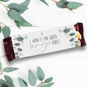 Puede incluir: Un envoltorio de barra de chocolate blanco con un diseño de hojas de eucalipto verdes y el texto "WHEN IT TAKES LONGER..." en letra negra.
