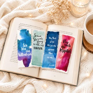 Op de afbeelding: Vier rechthoekige papieren bladwijzers met aquarelachtergronden en zwarte tekst. De bladwijzers bevatten de zinnen: Ich bin ein Kettenleser, Some Stories stay with us FOREVER, Das Buch ist die Axt für das gefrorene Meer in uns, en Nur noch ein Kapitel.