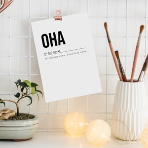 May include: A white card with the word "OHA" in bold black letters, followed by the phonetic pronunciation "[o:ha]" and the definition "Ausruf Norddeutsche Panikattacke". The card is pinned to a white grid wall with a gold clip.