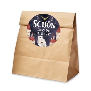 May include: A brown paper bag with a round sticker featuring a white owl with a letter in its beak. The sticker has a dark blue background with white stars and the text "SCH&Ouml;N DASS DU DA WARST".