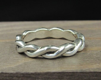 May include: A silver braided ring with a smooth, polished finish. The ring is made of a single piece of metal that is twisted and woven together to create a unique and intricate design.