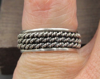 May include: A silver ring with a braided design. The ring is worn on a finger.