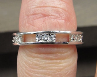 May include: A silver band ring with a clear stone set in the centre and smaller clear stones set around the band.