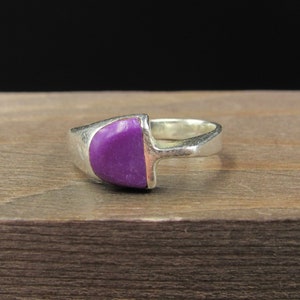 May include: A silver ring with a purple stone set in the center. The stone is shaped like a half-circle.