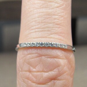 May include: A thin silver band with a row of small diamonds set in the metal.