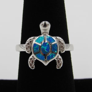 May include: A silver ring featuring a blue opal turtle design.