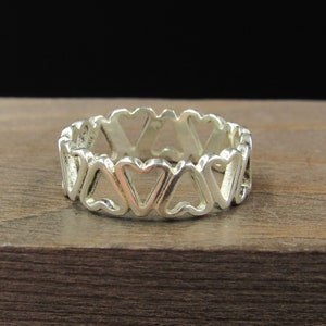 May include: A silver ring with a heart design. The ring is made of a series of connected hearts.