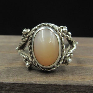 May include: A silver ring with a light pink oval gemstone set in a rope-like design.