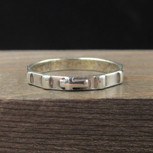 May include: A silver ring with a cross design. The ring is simple and elegant.