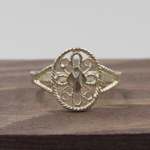 May include: A silver filigree ring with a delicate, intricate design. The ring is oval-shaped and has a floral pattern.