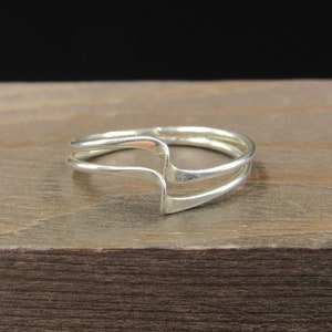 May include: A silver ring with a double band design. The band is curved and has a unique shape.