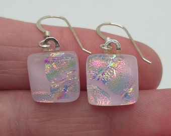 May include: A pair of silver dangle earrings with square iridescent pink glass charms. The earrings have a simple design and are perfect for everyday wear.
