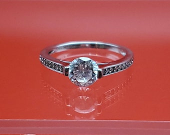 May include: A silver ring with a single round diamond in the centre and a row of smaller diamonds around the band.