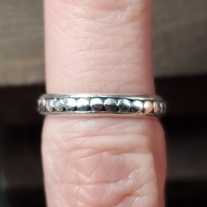 May include: A silver ring with a beaded design. The ring is worn on a finger.
