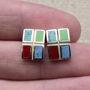 May include: A pair of rectangular stud earrings featuring a grid of four inlaid stones. Each earring contains a light blue turquoise piece, a solid green stone, a bright red stone, and a textured light blue stone set in a gold-toned metal frame.