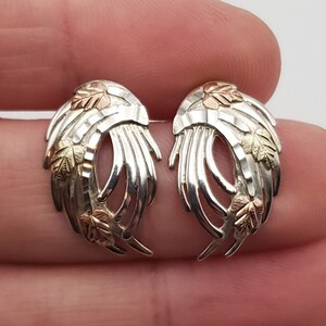 May include: A pair of silver earrings with a leaf design. The leaves are made of gold and green enamel.