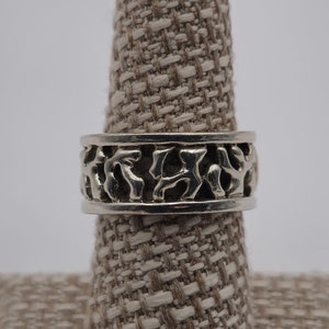 May include: A silver ring with a textured, organic design. The ring is displayed on a fabric ring holder.
