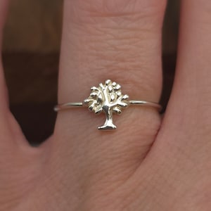 May include: A silver ring with a delicate tree design. The ring is on a person's finger.