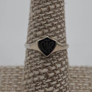 May include: A silver ring with a black shield-shaped design featuring the letters "CJR" in the center.