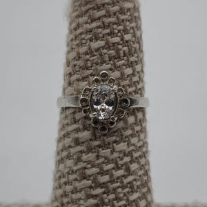 May include: A silver ring with a clear oval-shaped stone set in a decorative flower design.