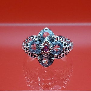 May include: A silver ring with a cluster of clear and pink gemstones set in a filigree design.