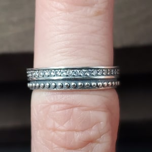 May include: Two silver rings with a beaded design. The top ring has a row of small, clear stones.