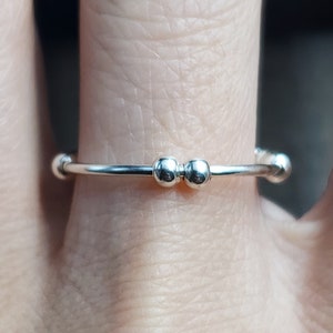 May include: A silver ring with two small round beads on the top.