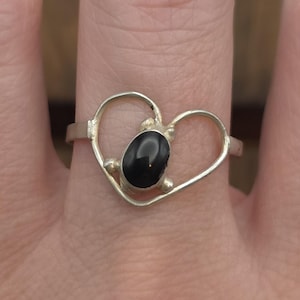 May include: A silver ring with a heart-shaped design featuring a black gemstone in the center.