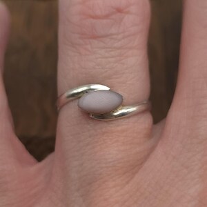 May include: A silver ring with a light pink oval-shaped stone set in a twisted band.