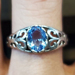 May include: A silver ring with a blue oval gemstone set in a filigree design.