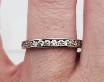 May include: A thin silver band with a row of small, clear diamonds set in a channel setting.