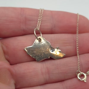 May include: A silver necklace with a pendant shaped like the state of Hawaii. The pendant has a small, clear stone in the center.