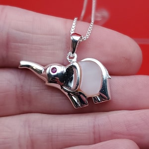 May include: A silver necklace with a white mother of pearl elephant pendant with a pink stone for an eye.