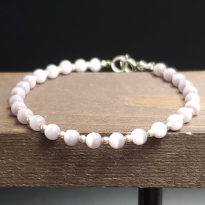 May include: A delicate bracelet made with small, round, light purple beads and silver accents.