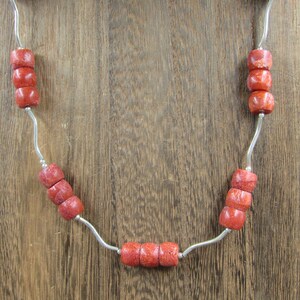 May include: A silver necklace with red coral beads. The necklace is displayed on a wooden stand.