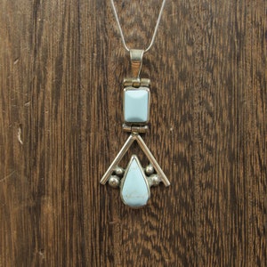 May include: A silver pendant necklace with a light blue turquoise stone. The pendant is shaped like a teardrop with a square stone at the top.