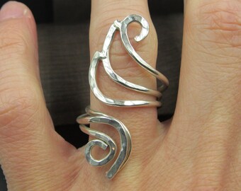 May include: A silver ring with a unique, abstract design. The ring is made of multiple intertwined bands that form a swirling, organic shape.